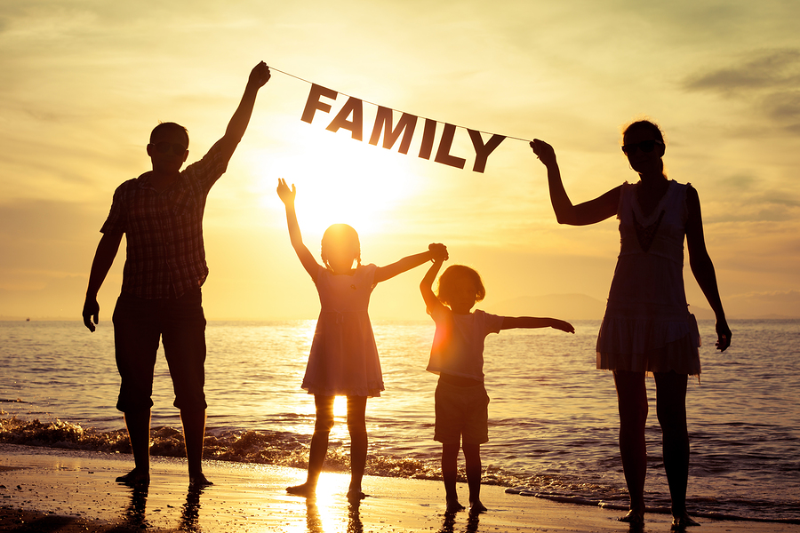 Happy family standing on the beach at the sunset time. Parents hold in the hands inscription "Family". Concept of happy family.